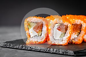 Appetizing sushi roll california with salmon cucumber cheese and masago caviar on a black stone plate