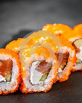 Appetizing sushi roll california with salmon cucumber cheese and masago caviar on a black stone plate
