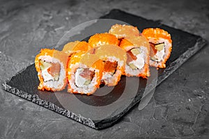 Appetizing sushi roll california with salmon cucumber cheese and masago caviar on a black stone plate