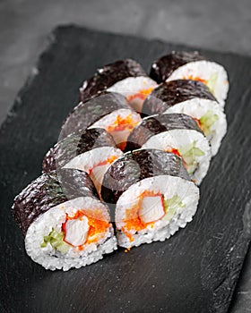 Appetizing sushi roll futomaki with cucumber crab stick and masago on a black stone plate