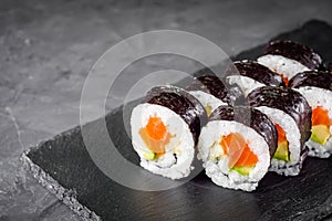 Appetizing sushi roll futomaki with cucumber and salmon on a black stone plate