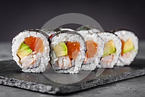 Appetizing sushi roll futomaki salmon, shrimp and avocado on a black stone plate