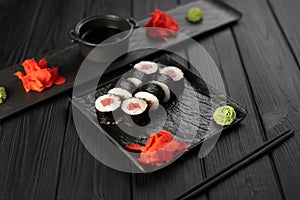 appetizing sushi roll futomaki with tuna on a black stone plate with sauce, ginger and wasabi.