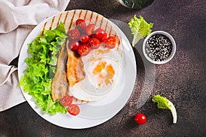 Appetizing tacos with fried egg, bacon, tomato and lettuce on a plate on the table top view