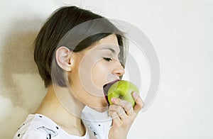 A girl with a short hair eats a green apple.