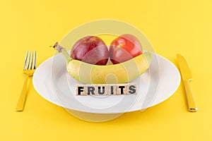 Apple, a banana and a tomato on a plate and the word 'fruits' written on wooden blocks