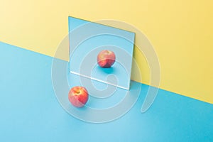 Apple on blue table over yellow background near mirror