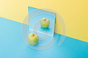 Apple on blue table over yellow background near mirror