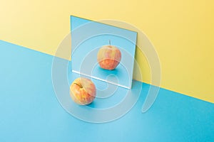 Apple on blue table over yellow background near mirror