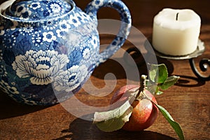 An apple, a blue teapot, a candle with holder on wooden table