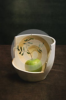 An apple with a branch of a plant inside a broken pot