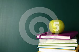 Apple with carved number five as school grade on books near green chalkboard, space for text