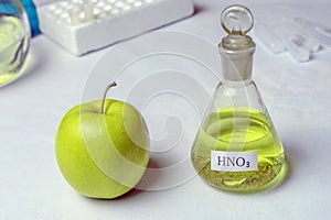 An apple and a chemical flask labeled nitric acid - nitrate. The concept of the presence of nitrates and GMOs photo