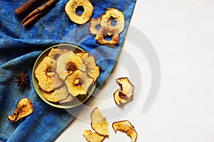 Apple chips and cinnamon on white wooden table. Homemade dry dehydrated fruit slices, autumn fall snack, healthy vegetarian diet