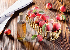 Apple cider vinegar in a glass bottle, fresh apples in a wicker basket, on a countertop made of old wood. Green leaf.