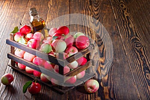 Apple cider vinegar in a glass bottle, fresh apples in a wooden box, on a countertop made of old wood. Green leaf.