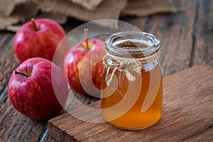 Apple cider vinegar in glass bottle and fresh red apples on wooden table