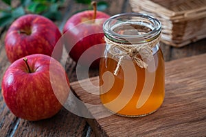 Apple cider vinegar in glass bottle and fresh red apples on wooden table