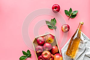 Apple cider vinegar in glass bottle and wooden tray with red apples