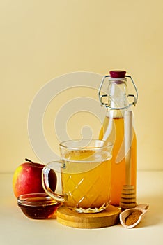 Apple Cider Vinegar in Glass Mug and Bottle with Honey and Cinnamon Red Apples Yellow Background Vertical