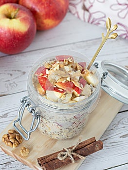 Apple cinnamon overnight oats with peanut butter and walnuts in a jar with a golden spoon on wooden background, vertical shot