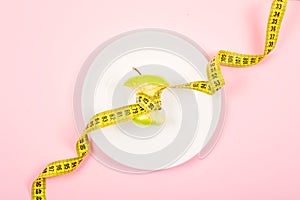 Apple core with measuring tape in place of the waist on a white plate on pink background. Diet, weigh loss, starvation, fitness