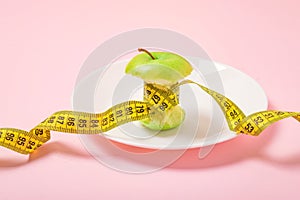 Apple core with measuring tape in place of the waist on a white plate on pink background. Diet, weigh loss, starvation, fitness photo