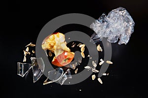 Apple core, polyethylene and glass shards on a black background with reflection. Ecology and waste recycling concept