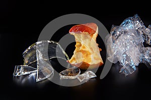 Apple core, polyethylene and glass shards on a black background with reflection. Ecology and waste recycling concept