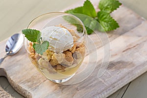 Apple crumble topping vanilla ice cream served with melisa in glass and wooden tray on table. photo
