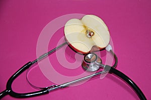 Apple cut in half with stethoscope on a pink background.