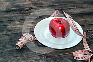 An apple on an empty white plate with a tape measure to measure the figure. Diet and raw food concept.