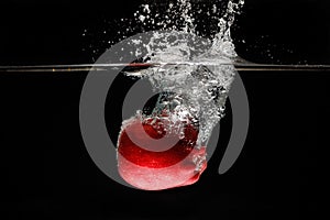 A apple falls deeply under water with a big splash.