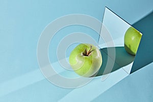 The apple is green, a square mirror on a blue background, a reflection of an apple and from shadows in a mirror.