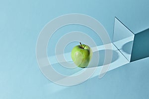 The apple is green, a square mirror on a blue background, a reflection of an apple and from shadows in a mirror.