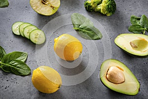 Apple, half  avocado halves with a stone,  broccoli, fresh green spinach leaves, yellow lemon  cucumber slices  on a gray