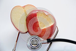 Apple with heart symbol cut from apple peel, with stethoscope on a white background, top view.