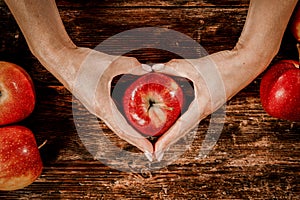 An apple held in female hands. Wooden table with blurred apples background. Empty spacer y foour decoration and products.