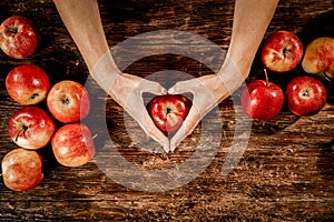 An apple held in female hands. Wooden table with blurred apples background. Empty spacer y foour decoration and products.