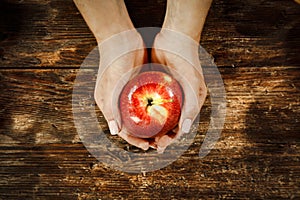 An apple held in female hands. Wooden table with blurred apples background. Empty spacer y foour decoration and products.