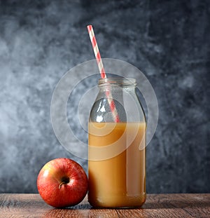 Apple juice in the bottle with drinking straw - gray background