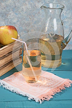 Apple juice in a glass, juice in a jug, apples in a wooden box, colored wooden background.