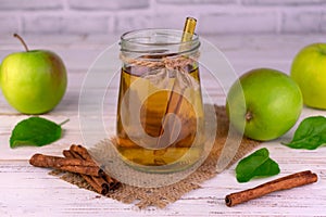 Apple juice in a jar and fresh green apples with cinnamon sticks.