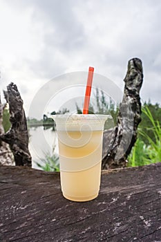 Apple juice in plastic cup on wooden table on lake background