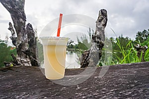 Apple juice in plastic cup on wooden table on lake background