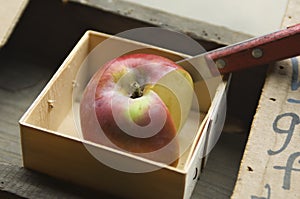 Apple and knife in a wooden box for produce sampling.