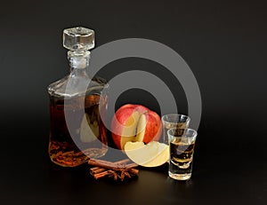 Apple liqueur with cinnamon, anise and ripe apple slices on a black background in a bottle and two glasses