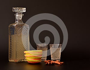 Apple liqueur with spices on a black background, homemade alcohol in a crystal decanter and two glasses, cinnamon sticks, anise