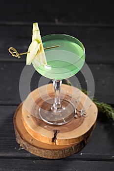 Apple Martini cocktail with garnish on wooden board on black table