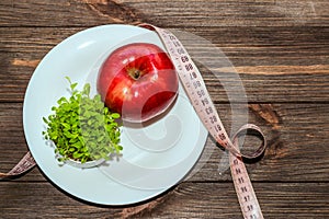 An apple with microgreen on an empty white plate with a tape measure to measure the figure. Diet and raw food concept.